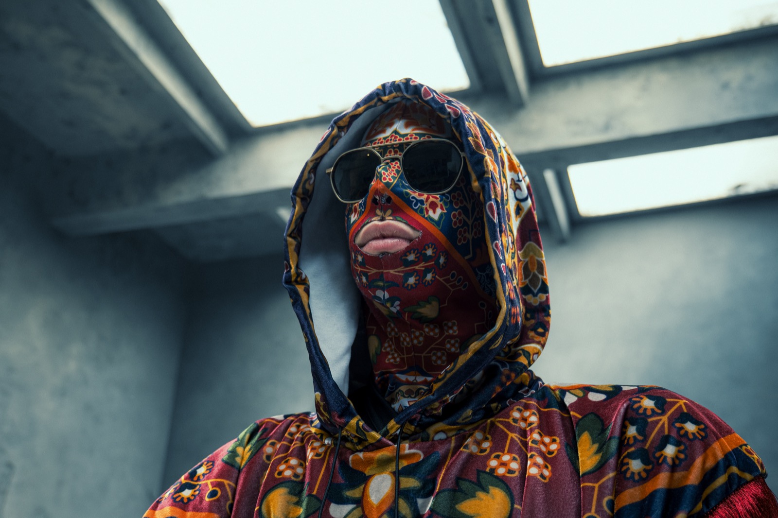 Carpetman in his carpet-pattern mask and hood, looking up under a concrete skylight